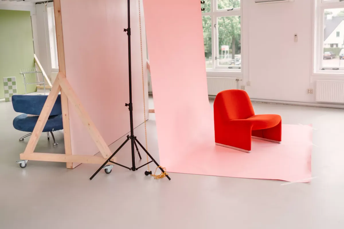 Club MALO met verrijdbare gekleurde wanden, daglicht en een rode stoel op een roze papieren achtergrond