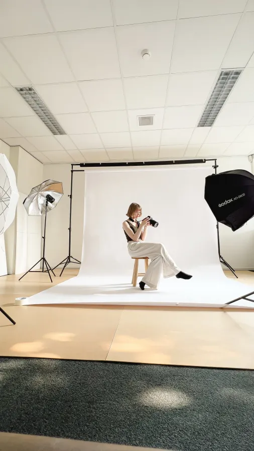Opnameset van Sara Roos met witte achtergrond, kruk, fotograaf en meerdere studiolampen