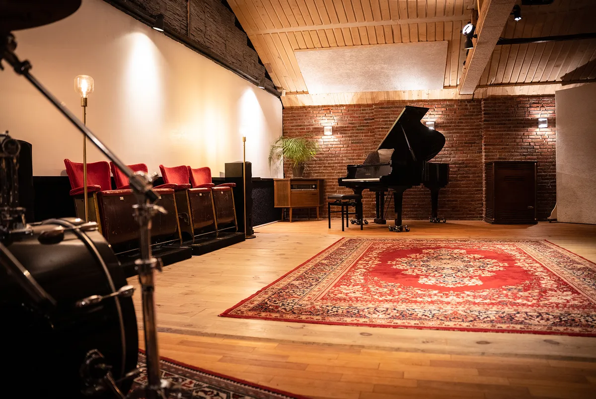 Live-room van Studio A60 met vleugel, drums, houten vloer en rode stoelen