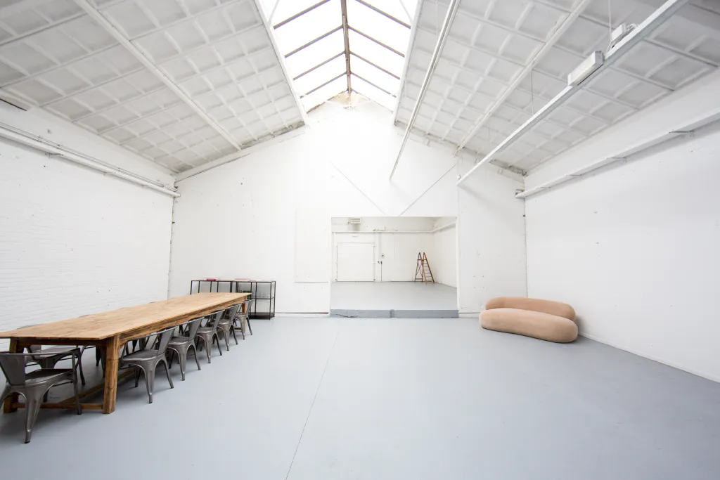 Lichte studio met dakramen, grote deuren, lange tafel en bank