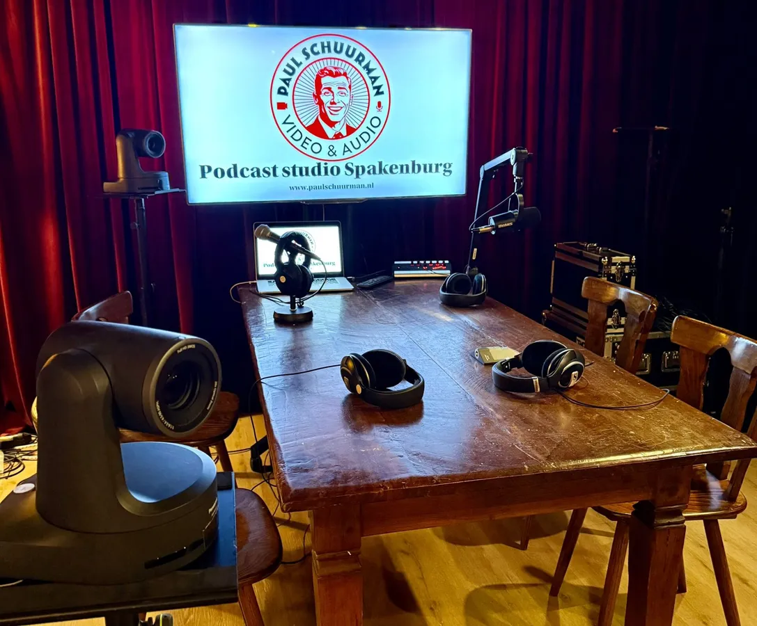 Podcaststudio van Paul Schuurman met tafel, stoelen, microfoons, camera’s en scherm